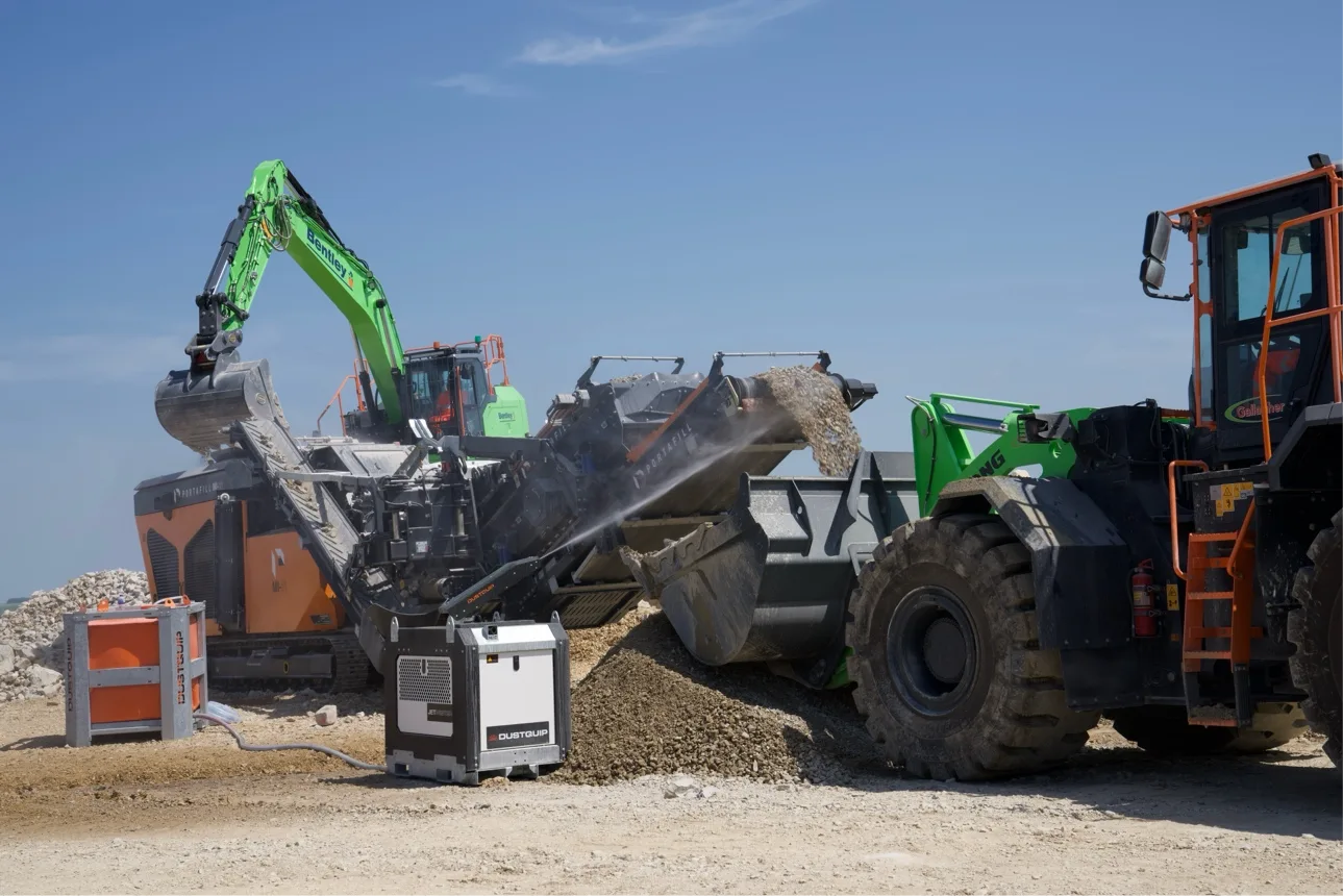 A man sits in the cab of a yellow LiuGong excavator talking with a group of visitors gathered around the machine at the show.