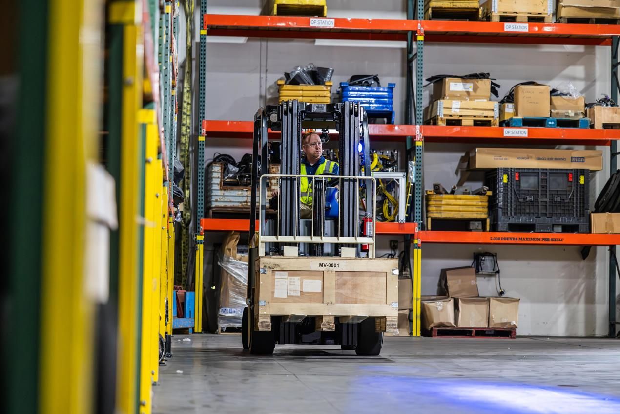 Yale electric lift truck viewed head-on carrying a large wooden crate down a warehouse aisle