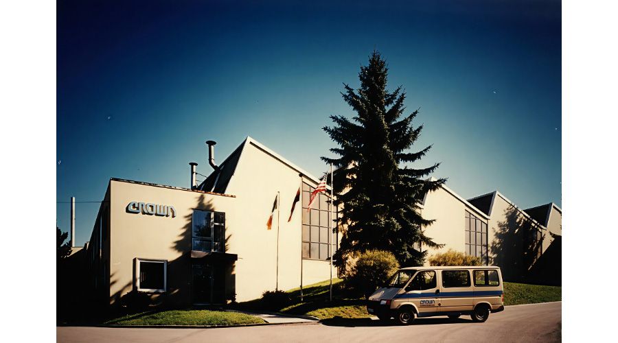 Archive-style view of the original Crown Roding plant, a pale angular building with Crown signage, a tall conifer and a Crown-branded van parked outside under a clear sky