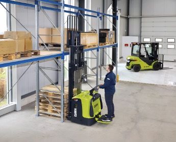 A worker operating a green and black Clark high-lift truck at pallet racking in a warehouse, with a Clark counterbalance forklift in the background