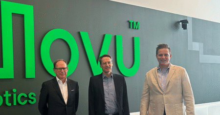 Jungheinrich joins forces with Movu Robotics Three men in business dress stand in front of an illuminated green Movu Robotics wall sign