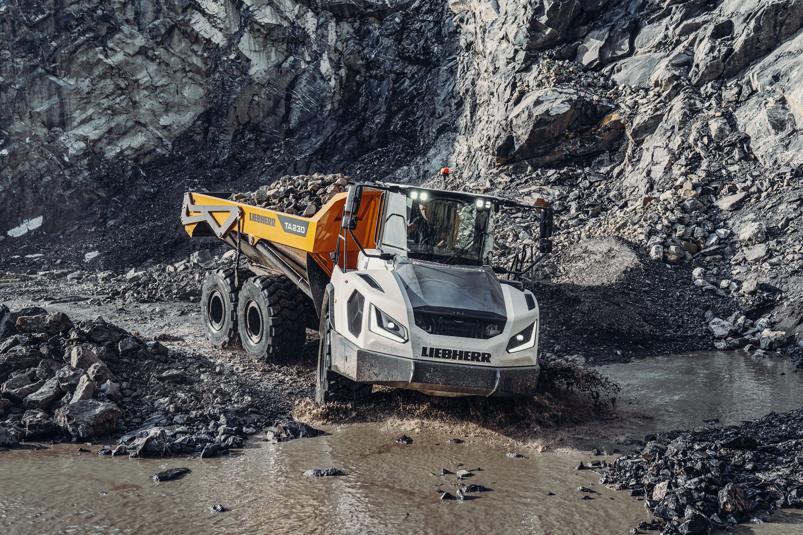 Liebherr TA 230 articulated dump truck loaded with rock driving through water in a quarry