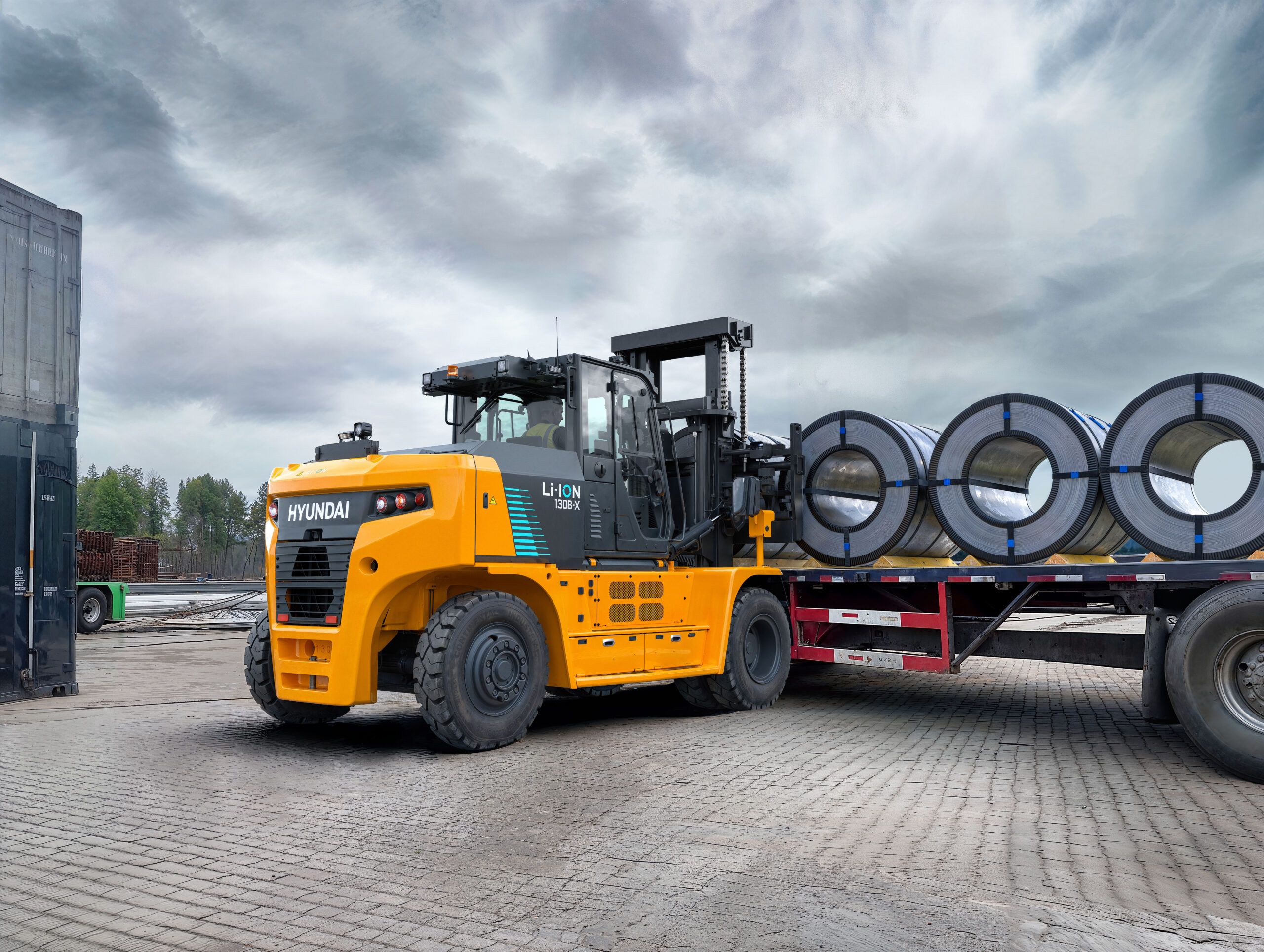 Hyundai 130B-X electric forklift loading steel coils onto a flatbed trailer