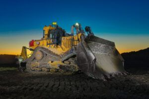 Cat D11 XE electric drive mining dozer with a loaded blade, photographed at dusk against an orange and blue sky, with “D11 XE” and “electric drive” badging visible on the machine