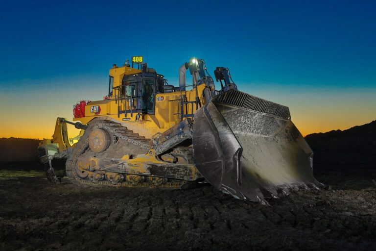 Cat D11 XE electric drive mining dozer with a loaded blade, photographed at dusk against an orange and blue sky, with “D11 XE” and “electric drive” badging visible on the machine