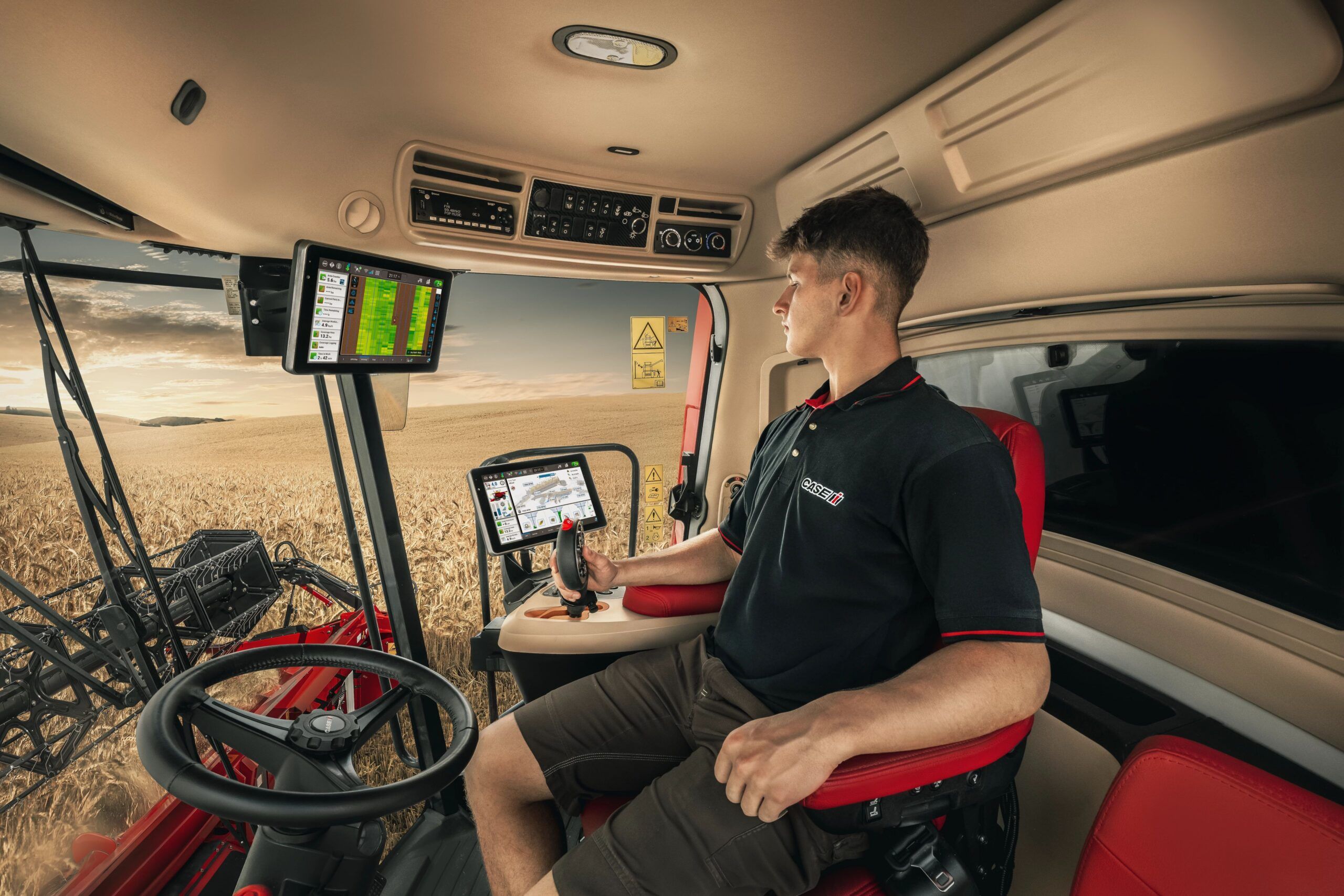 Interior of a Case IH Axial-Flow combine cab, with an operator seated at the controls and two Pro 1200 touchscreen displays showing field and machine data, a wheat field visible through the windscreen at sunset.