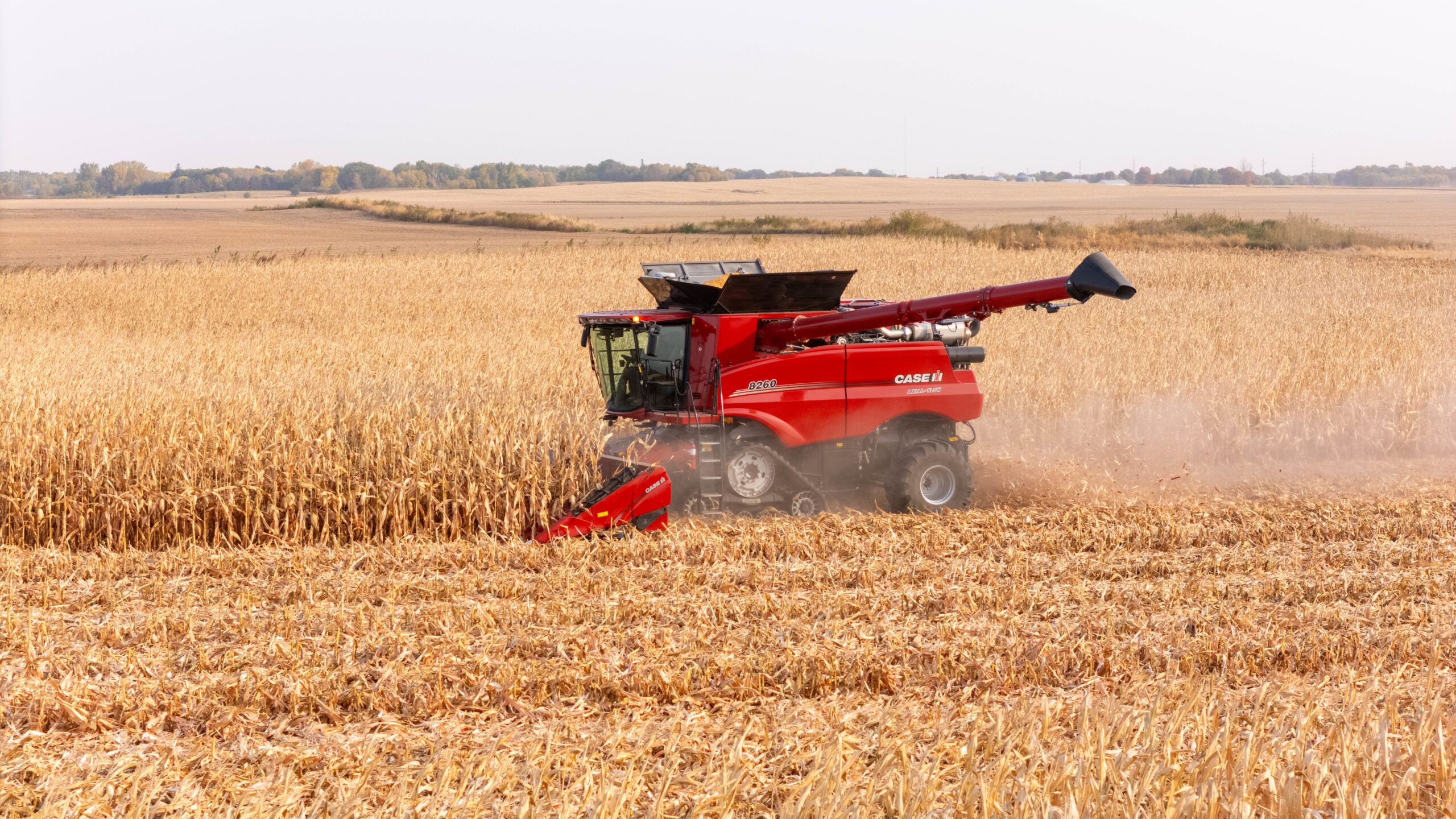 A red Case IH Axial-Flow combine parked in a harvested field at sunset with its draper header lowered and grain-tank covers open, against a dramatic evening sky.