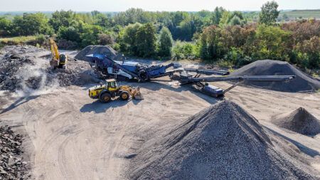 Kleemann reveals MR 130 Evo successor for 2027 Blue Kleemann MOBIREX MR 130 EVO tracked mobile impact crusher operating on an outdoor recycling site, feeding a long tracked stacking conveyor with graded aggregate stockpiles alongside