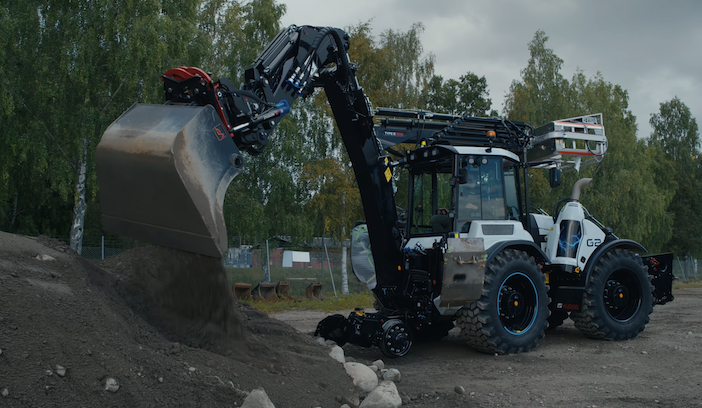 Huddig excavator loader using its rear bucket attachment to move soil and stones on an outdoor construction site.