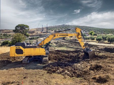 Liebherr expands 50-tonne crawler excavator range Yellow Liebherr R 948 G8 crawler excavator digging soil on open earthmoving ground, with olive groves and piling rigs on the hills behind.