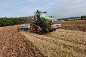 Green Fendt 1100 Vario MT tracked tractor working a stubble field with a mounted cultivator behind it, under a blue sky