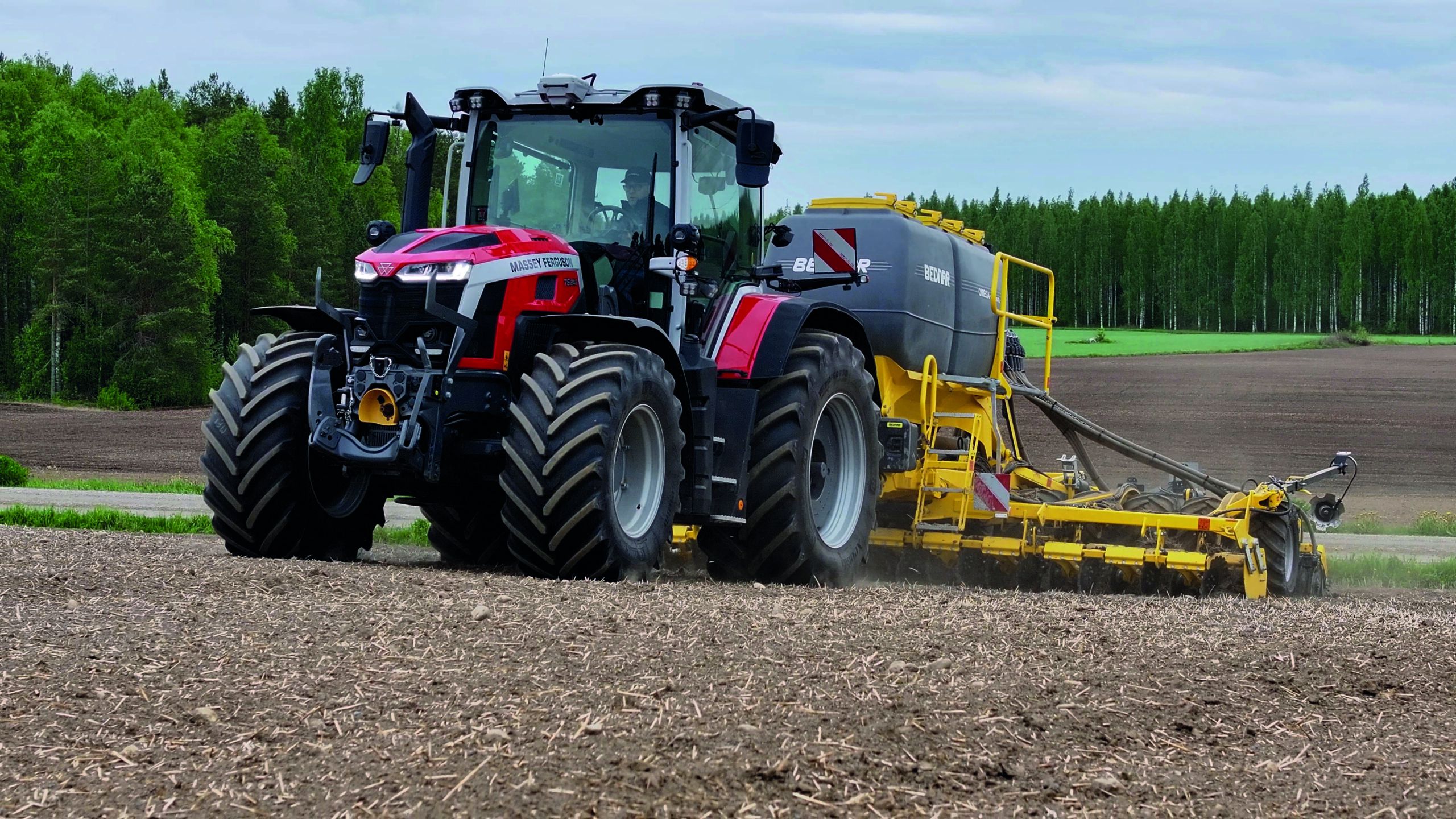 Massey Ferguson 7S Mark 2 tractor working cultivated soil in front of a forest, front three-quarter view.