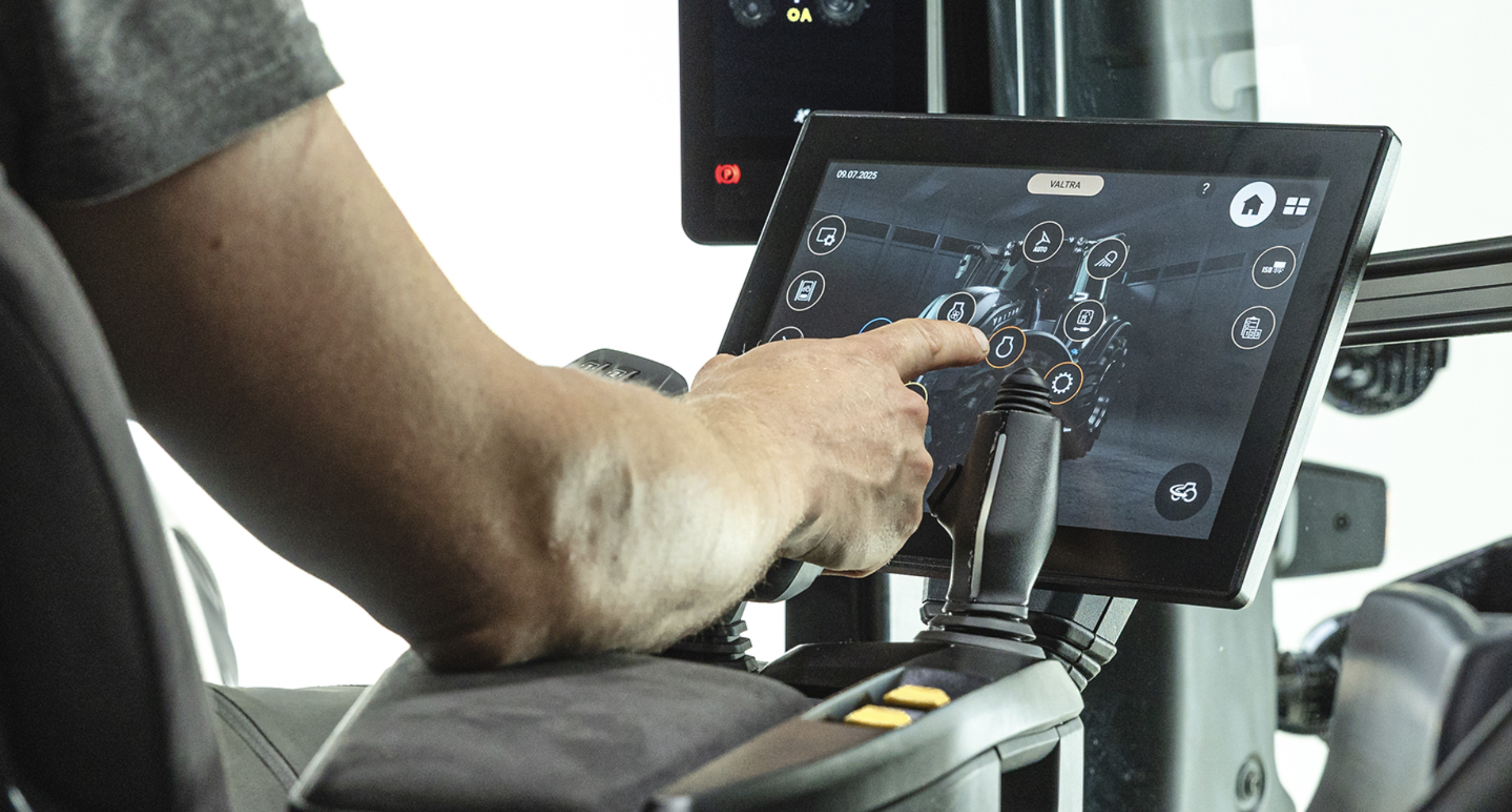 Operator reaching to a 12in SmartTouch Gen2 touchscreen in a Valtra T Series cab, with armrest-mounted joystick controls in the foreground.