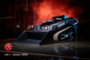 A dark blue Bobcat RogueX3 concept track loader with a raised bucket, lit dramatically against red smoke in an industrial setting, with a Red Dot winner 2026 logo in the lower corner.