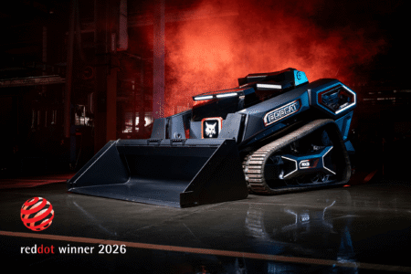Bobcat’s RogueX3 autonomous concept loader earns Red Dot award A dark blue Bobcat RogueX3 concept track loader with a raised bucket, lit dramatically against red smoke in an industrial setting, with a Red Dot winner 2026 logo in the lower corner.